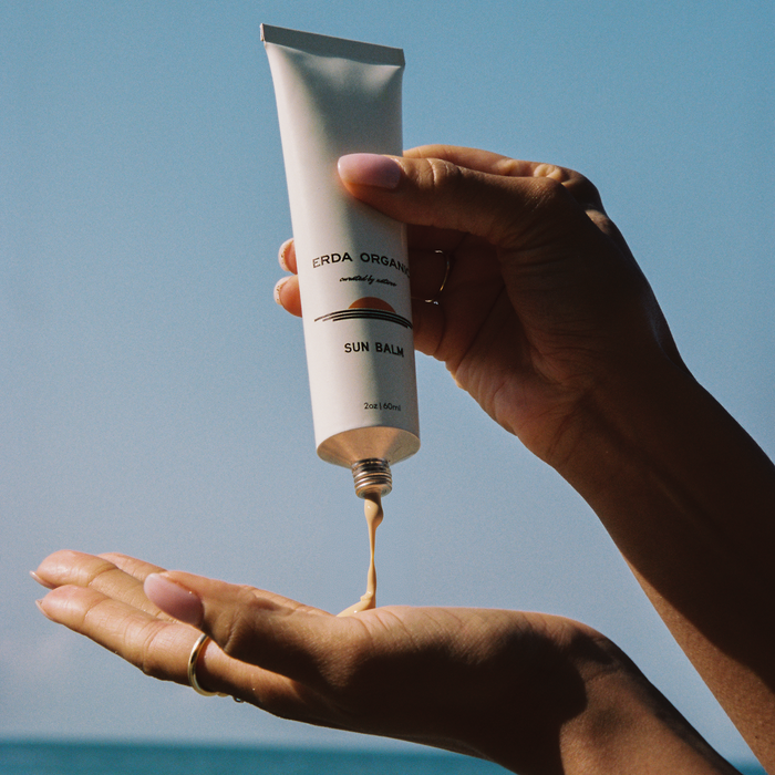 Hand holding a tube of sunscreen with a beach in the background