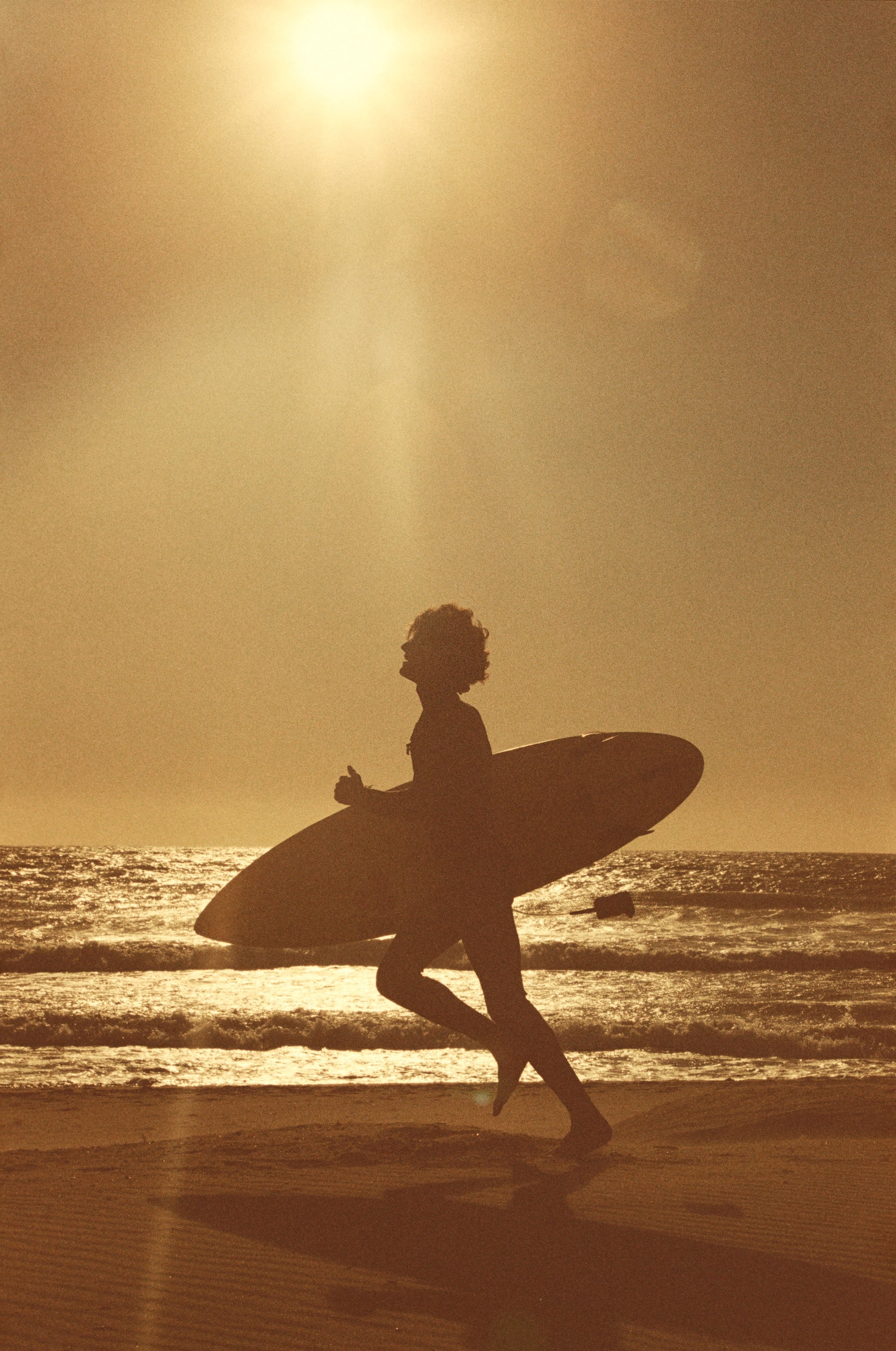 SURFER RUNNING ON THE BEACH AT SUNSET